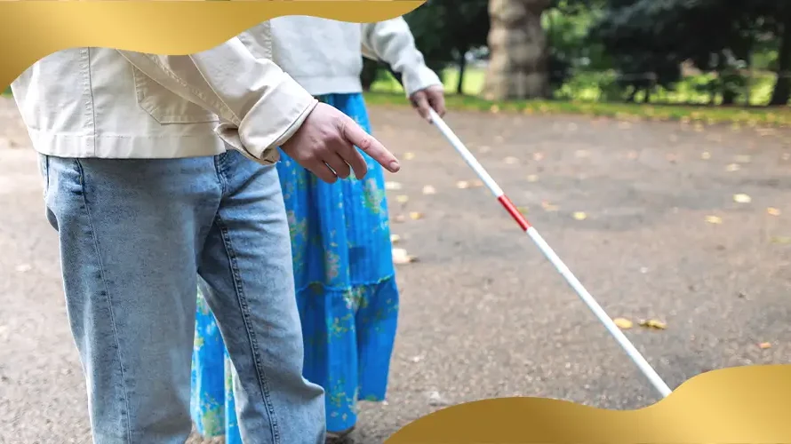 Visually impaired person using a white cane while walking with assistance on a park pathway, representing blindness, mobility support, and vision impairment awareness.