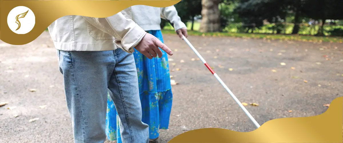 Visually impaired person using a white cane while walking with assistance on a park pathway, representing blindness, mobility support, and vision impairment awareness.