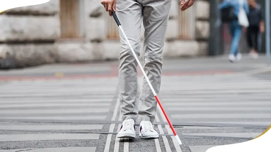 Person with visual impairment walking with a white cane across a crosswalk, symbolizing blindness and mobility support