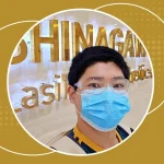 Smiling man wearing a face mask and goggles inside Shinagawa Lasik & Aesthetics Center, standing in front of the clinic’s gold signage