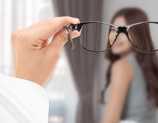 View through eyeglasses showing a sharp image of a woman in front, with the surrounding vision blurred—illustrating the clarity provided by corrective lenses