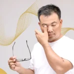 Man rubbing his eyes while holding eyeglasses, showing discomfort or signs of eye strain possibly related to vision issues