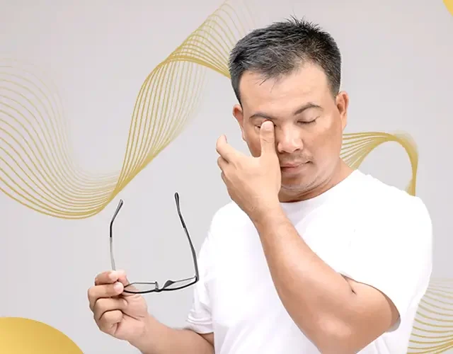 Man rubbing his eyes while holding eyeglasses, showing discomfort or signs of eye strain possibly related to vision issues