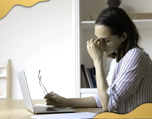 Woman experiencing eye strain while working on a laptop, indicating possible digital eye fatigue or vision issues related to prolonged screen use