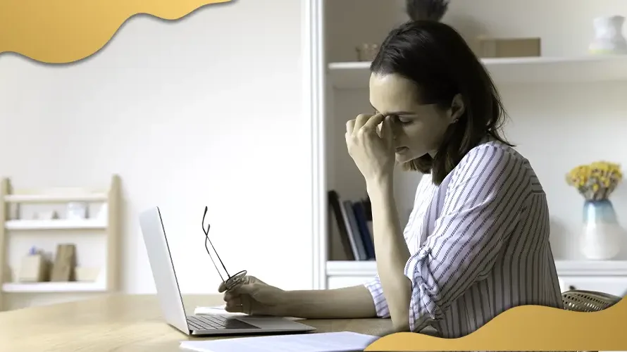 Woman experiencing eye strain while working on a laptop, indicating possible digital eye fatigue or vision issues related to prolonged screen use