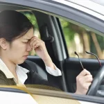 Woman sitting in a car rubbing her eyes from blurry vision or eye strain, suggesting possible keratoconus or vision issues while driving