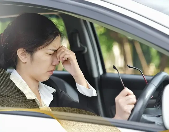 Woman sitting in a car rubbing her eyes from blurry vision or eye strain, suggesting possible keratoconus or vision issues while driving