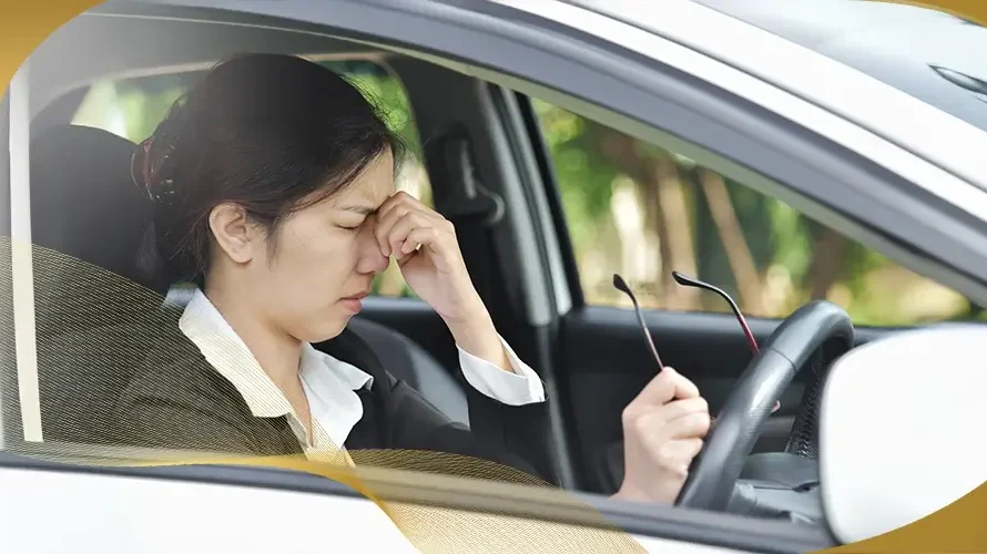 Woman sitting in a car rubbing her eyes from blurry vision or eye strain, suggesting possible keratoconus or vision issues while driving