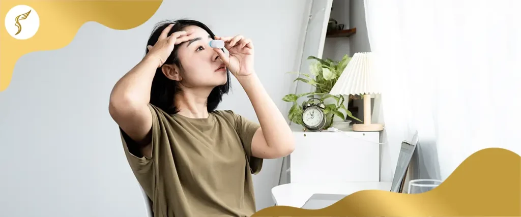 Woman applying eye drops at home to relieve dry eyes and eye strain while working on a laptop.