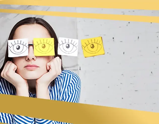 Woman wearing paper cutouts of eyes over her glasses, symbolising blurred or distorted vision linked to eye conditions like keratoconus