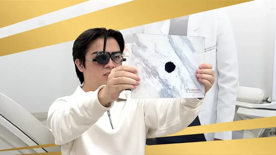 Patient undergoing eye exam at Shinagawa Lasik & Aesthetics using occluder glasses and pinhole test chart to assess visual acuity and refractive errors.
