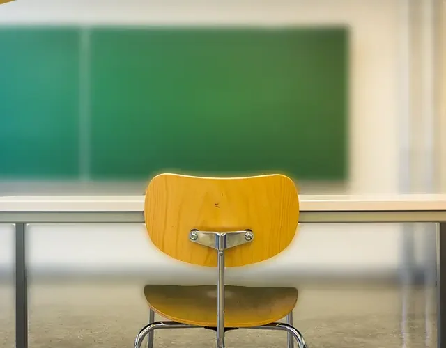Empty classroom desk and chair facing green chalkboard in school room.