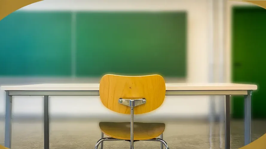 Empty classroom desk and chair facing green chalkboard in school room.